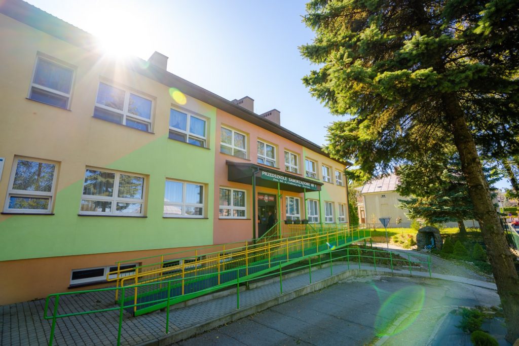 Dwukondygnacyjny budynek przedszkola z podjazdem dla wózków inwalidzkich. Elewacja budynku kolorowa.