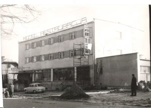 Czarno-białe zdjęcie z budowy hotelu i restauracji. Przed budynkiem stoi samochów
